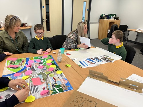 A group of people, including adults and children, sitting around a table engaged in an activity with maps and colored sticky notes
