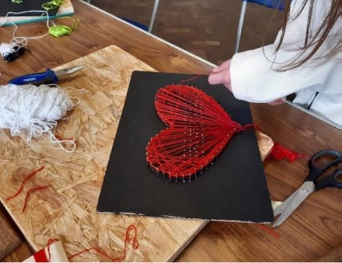 A child crafting a heart out of red strings.