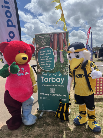 Mood Bear and Gilbert Gull mascots in front of a 'Foster with Torbay' poster.