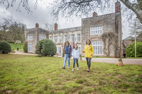 Two women and a girl walking happily in front of Cockington Court's Manor House.