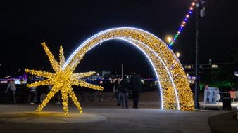 Illuminated star and arch light installation on Torquay seafront at night, with people walking beneath the lights